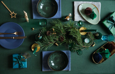 Christmas celebration table settings with winter holiday decorations on the green linen cloth.