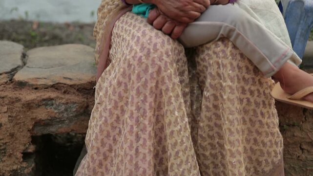 Video shot of village grandmother sitting on a stone side path in Uttarakhand villahe hoouse, smiling as she holds her grandchild during sunset, reflecting rural warmth, love, and simple Himalay
