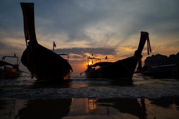 Beautiful view of silhouette of long-tail boats on the beach, sea and stunning sky during sunset at...