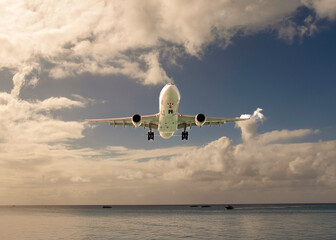 A dramatic view of a large white airplane from underneath over water against a blue sky with clouds