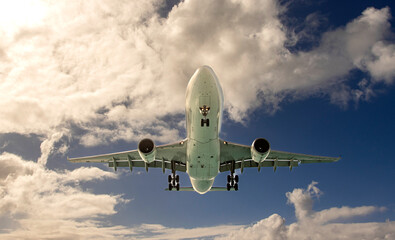 A dramatic view of a large white airplane from underneath against a bule sky with clouds