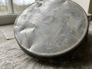 A Dented and Worn Tin Lid with Scratches and Rough Texture