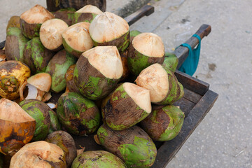 Fresh young coconuts displayed on a street market stall, with a vendor holding a peeled coconut. Tropical produce, natural textures and vibrant green and brown colors create an authentic Zanzibar 