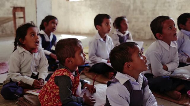 Raw video footage of Indian village school children attentively listening to teacher while sitting on classroom floor inside rural school in India.