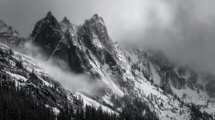 Majestic snowcapped mountain peaks shrouded in atmospheric mist and clouds, creating a dramatic black and white winter landscape