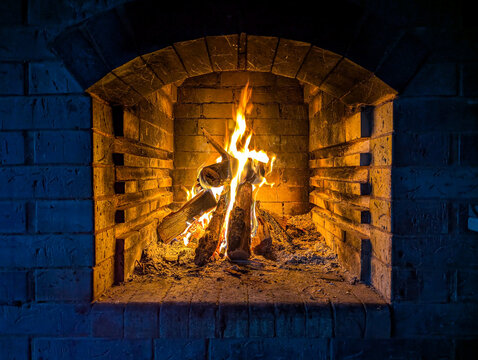 A fireplace recessed into a brick wall. A fire lit in the stove for cooking. A warm, cozy little space against the cold surroundings. Flames burst from the forge.