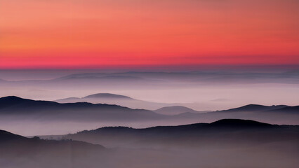 Fototapeta premium layered rolling hill silhouettes under terracotta red to pale lilac sunset