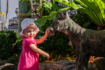 Little girl in pink dress touching stone sculpture in sunny park, joyful expression and curiosity, childhood innocence and learning concept