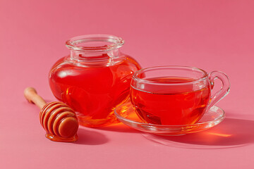 Słoiki i filiżanka z jaskrawo pomarańczowo-czerwoną cieczą (syrop lub mi&oacute;d) oraz drewniana łyżka na jasnor&oacute;żowym, jednolitym tle z ostrym światłem.