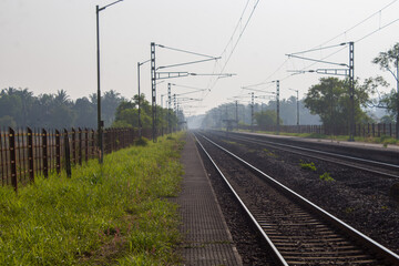 Morning view of a train moving along railway tracks, captured with soft mist and natural light at a...