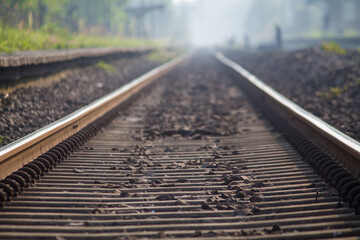 Morning view of a train moving along railway tracks, captured with soft mist and natural light at a quiet rural station.
