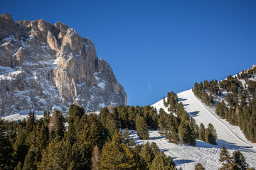 Sassolungo Rock with Snow Covered Ski Slope in South Tyrol. Winter Dolomites with Langkofel and Green Trees in Italy.