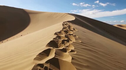 Expansive desert landscape featuring a towering sand dune with footprints leading across the crest under a bright blue sky - Powered by Adobe