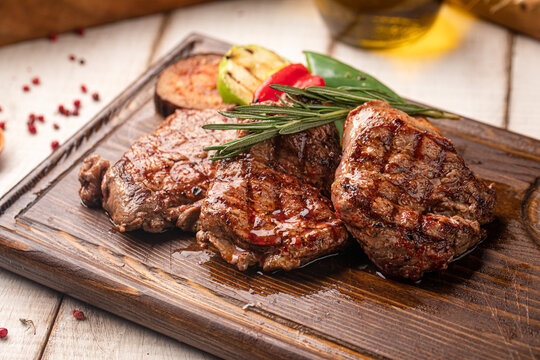 Juicy grilled beef steak portion served on a wooden board with roasted vegetables and herbs