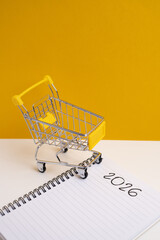 2026 Budgeting strategy. Miniature shopping cart and notebook for financial planning