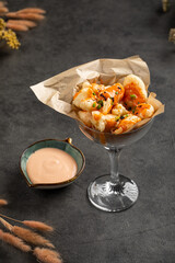 Golden crispy shrimp bites presented in glass cup with herbs and paired with creamy dipping sauce