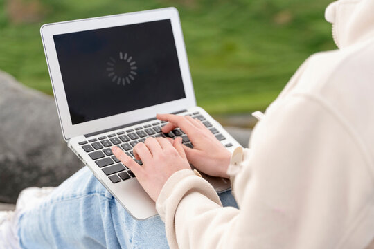 Person using laptop outdoors while waiting for loading screen - Powered by Adobe