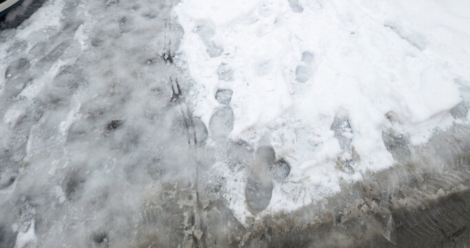 Footprints on snowy ground show traces of movement in a winter landscape, contrasting with icy patches underfoot. Ideal for seasonal and outdoor themes.