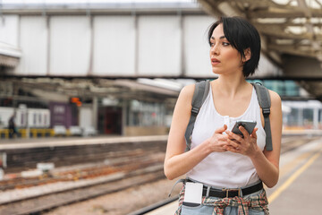 Young woman waiting at train station with smartphone