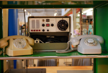 Fototapeta premium A vintage communication setup featuring rotary dial phones and an old control unit placed on a shelf. The equipment highlights classic technology and early communication systems. Ideal for
