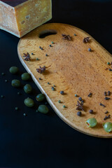 Aged cheese block, olives, and spices (star anise, pepper) arranged on a wooden board. Dark food photography still life. Perfect for recipes or gourmet menus
