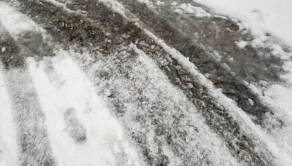 A close-up view of a snowy pathway with tire tracks, showcasing a blend of snow and ice. The scene captures a winter atmosphere and the impact of weather on travel.