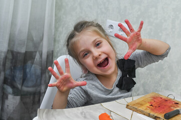 little girl in the kitchen makes funny faces while laughing joyfully, her hands completely red from beetroot juice. fun and messy reality of teaching children cooking skills at home.