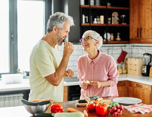 Portrait of happy senior mid aged mature couple prepering meal with fresh vegatebles in kitchen at hpme