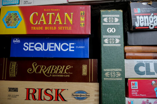 A stack of popular board games, including Catan, GO, Sequence, Scrabble, Risk, Jenga, and Clue. For Editorial Use Only.