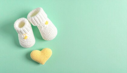 Minimalist Baby Announcement Flat Lay: White Knitted Booties and Yellow Crochet Heart on Mint Green.