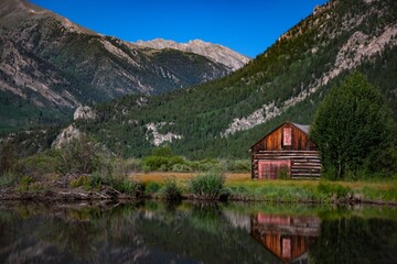Fototapeta premium Picturesque Old Barn nestled in the Mountains next to a Calm Lake