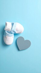 Soft White and Blue Baby Booties with Wooden Heart on Sky Blue Background. Newborn Boy Flat Lay Composition.