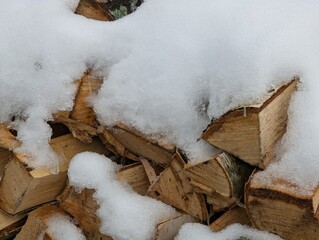 Country background with chopped birch firewood under snow.