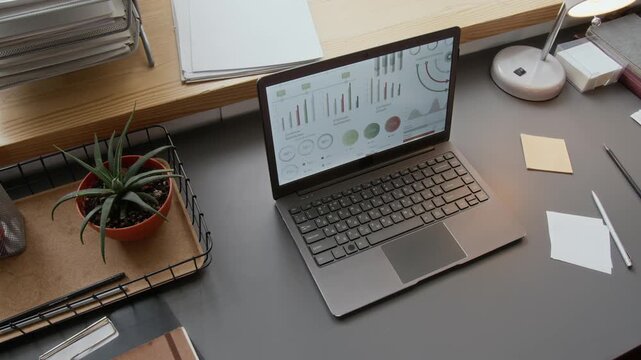 No people high angle shot of workspace with laptop, scattered papers, and potted plan in modern minimalist office