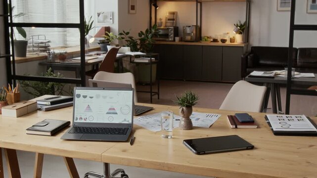 No people shot of interior of modern-well lit office space with wooden furniture and laptop with business charts on desk