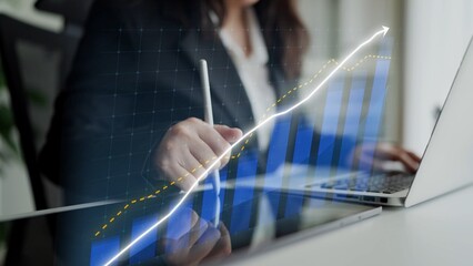 A business professional focuses on financial data analysis with digital graphs displayed on a laptop. The scene illustrates growth and productivity in a modern office setting. Copula