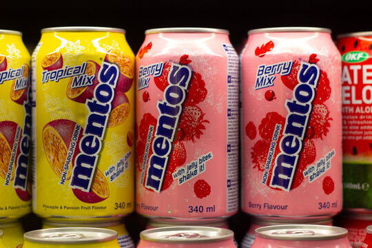 Yerevan, Armenia - November 8, 2025: Horizontal photo. Row of yellow, pink metal cans with sugar cold soft drink with tropical, berry flavor, Mentos logo on shelf of store, shop. Soda water, fast food