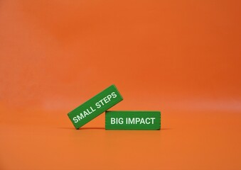 Two green blocks with 'Small Steps' and 'Big Impact' rest on an orange backdrop, illustrating how small actions build momentum, growth, and success in business and teamwork.