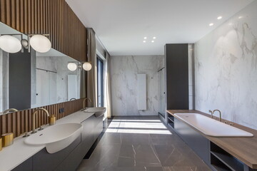 Spacious bathroom showcases minimalist design with double sinks, large mirror, and luxurious bathtub. Natural light streams in, enhancing the modern atmosphere and finishes