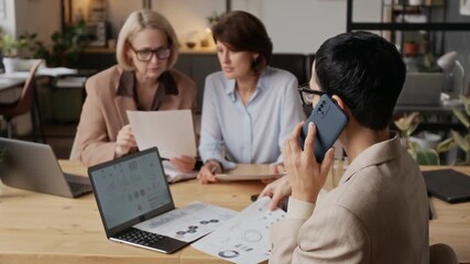 Middle-aged Caucasian woman with short hair having important business call, while her colleagues working with documents at desk in modern office - Powered by Adobe