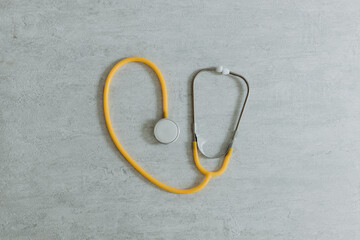One yellow stethoscope on a gray stone background.