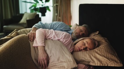 Married couple in their 50s sleeping embraced in comfortable bed, relaxation