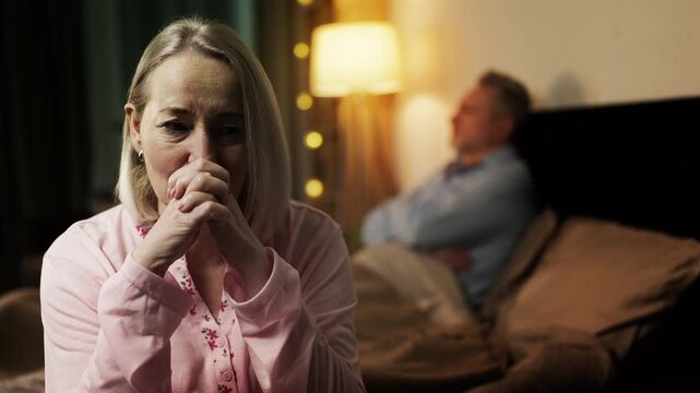 Sad middle-aged wife and husband sitting apart on bed, relationship crisis