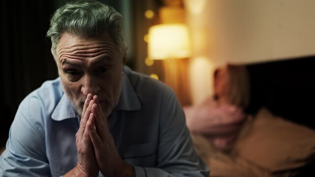 Upset middle-aged couple sitting separately on bed, signs of family conflict