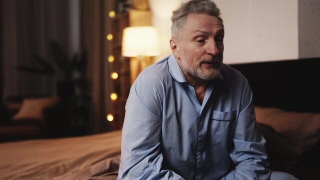 Upset middle-aged man sitting on bed and worrying about his health condition