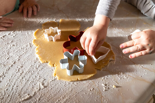 A family baking scene with children preparing German-style cut-out cookies. Little hands working with flour, dough, and festive cookie cutters.