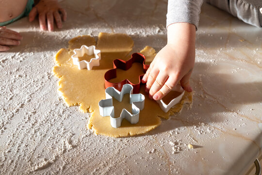 A family baking scene with children preparing German-style cut-out cookies. Little hands working with flour, dough, and festive cookie cutters.