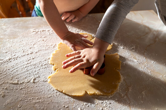 A family baking scene with children preparing German-style cut-out cookies. Little hands working with flour, dough, and festive cookie cutters.