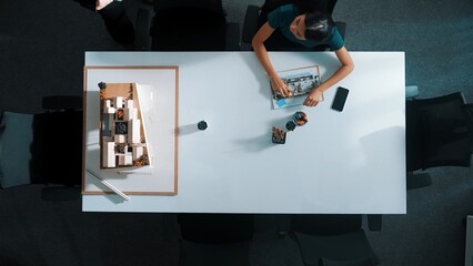 Top down aerial view of businesswoman writing and planning blueprint while sitting at meeting at...