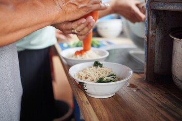 Traditional chicken noodle preparation with seasoning being added directly into the bowl.